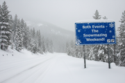 A very snowy mountain road sign that says "Both Events - The Snowmazing Weekend!"